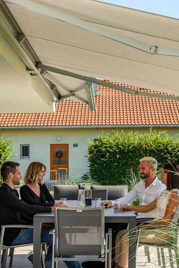 Vier Personen sitzen auf der Terrasse Tisch im Freien, unter einer Gelenkarmmarkise